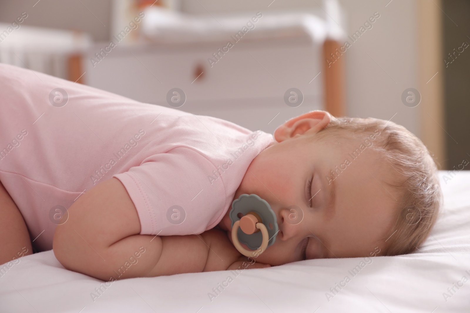 Photo of Adorable little baby with pacifier sleeping on bed at home