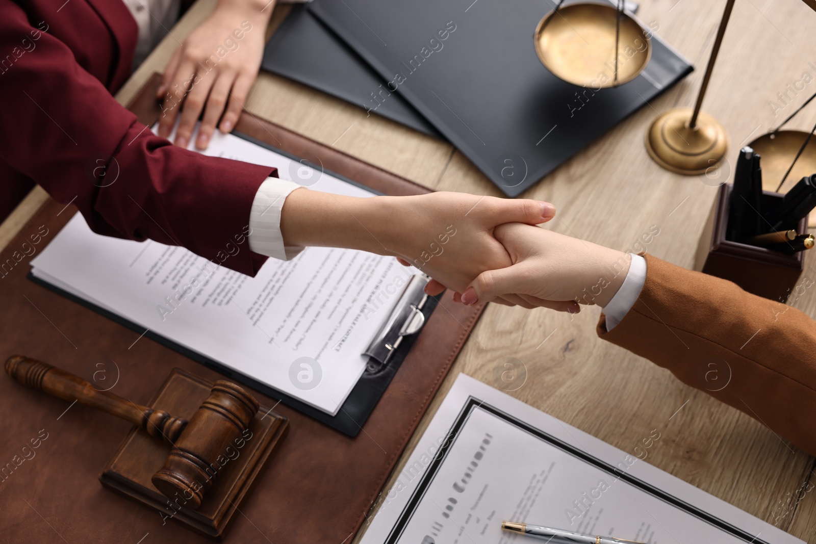 Photo of Notary shaking hands with client at wooden table, closeup