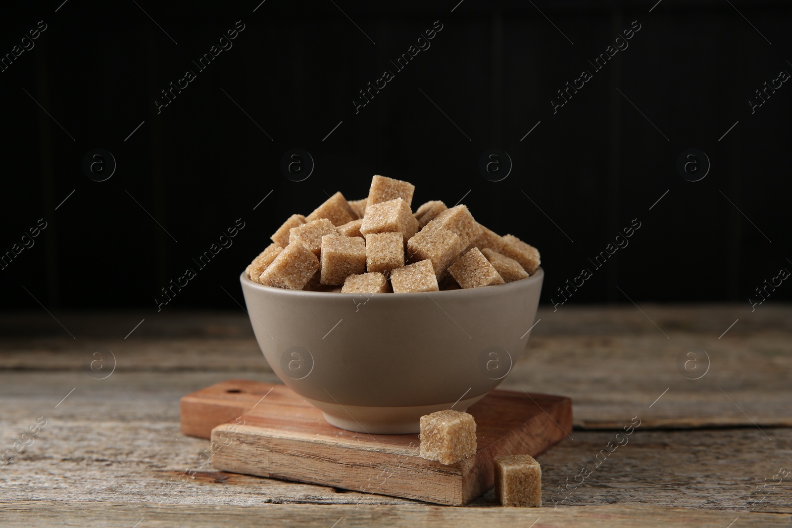 Photo of Bowl with brown sugar cubes on wooden table