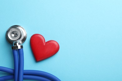 Stethoscope and red heart on light blue background, top view. Space for text