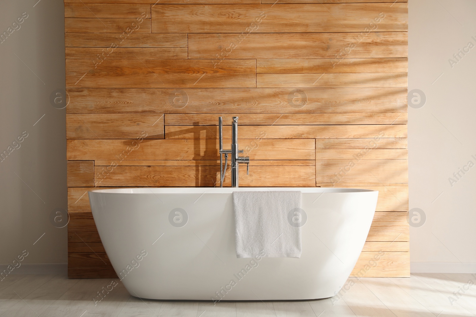 Photo of White bathtub with towel near wooden wall in room