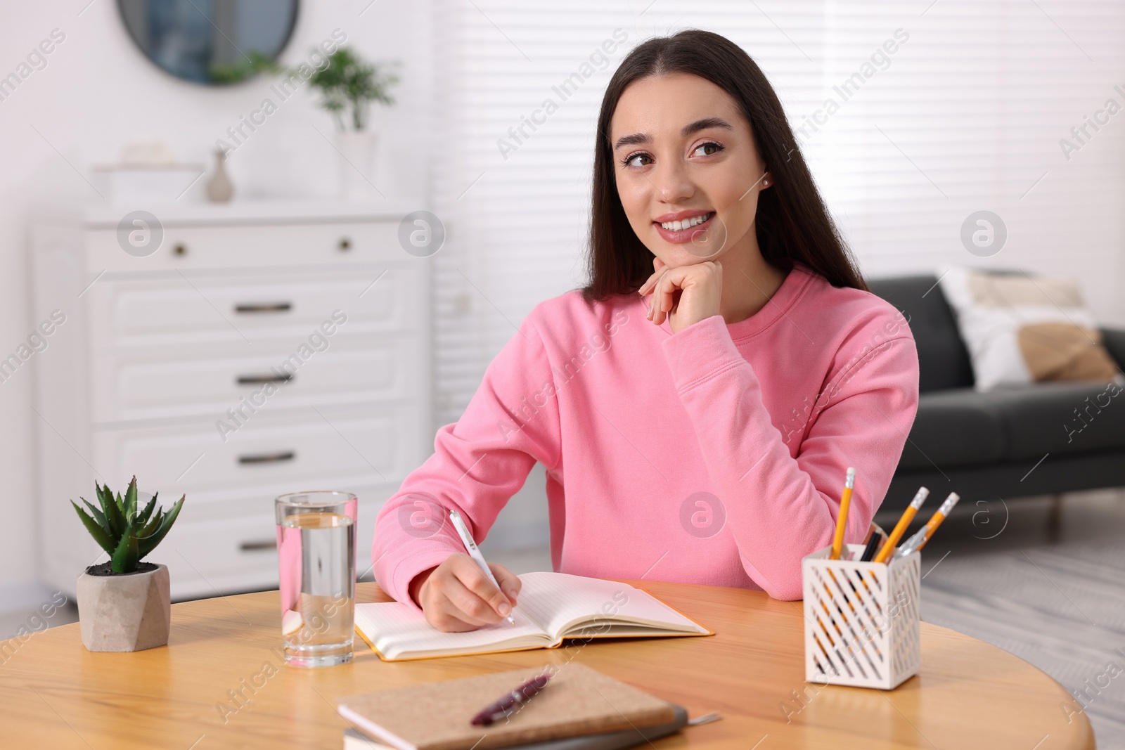 Photo of Young woman writing in notebook at wooden table indoors