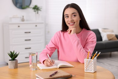 Photo of Young woman writing in notebook at wooden table indoors