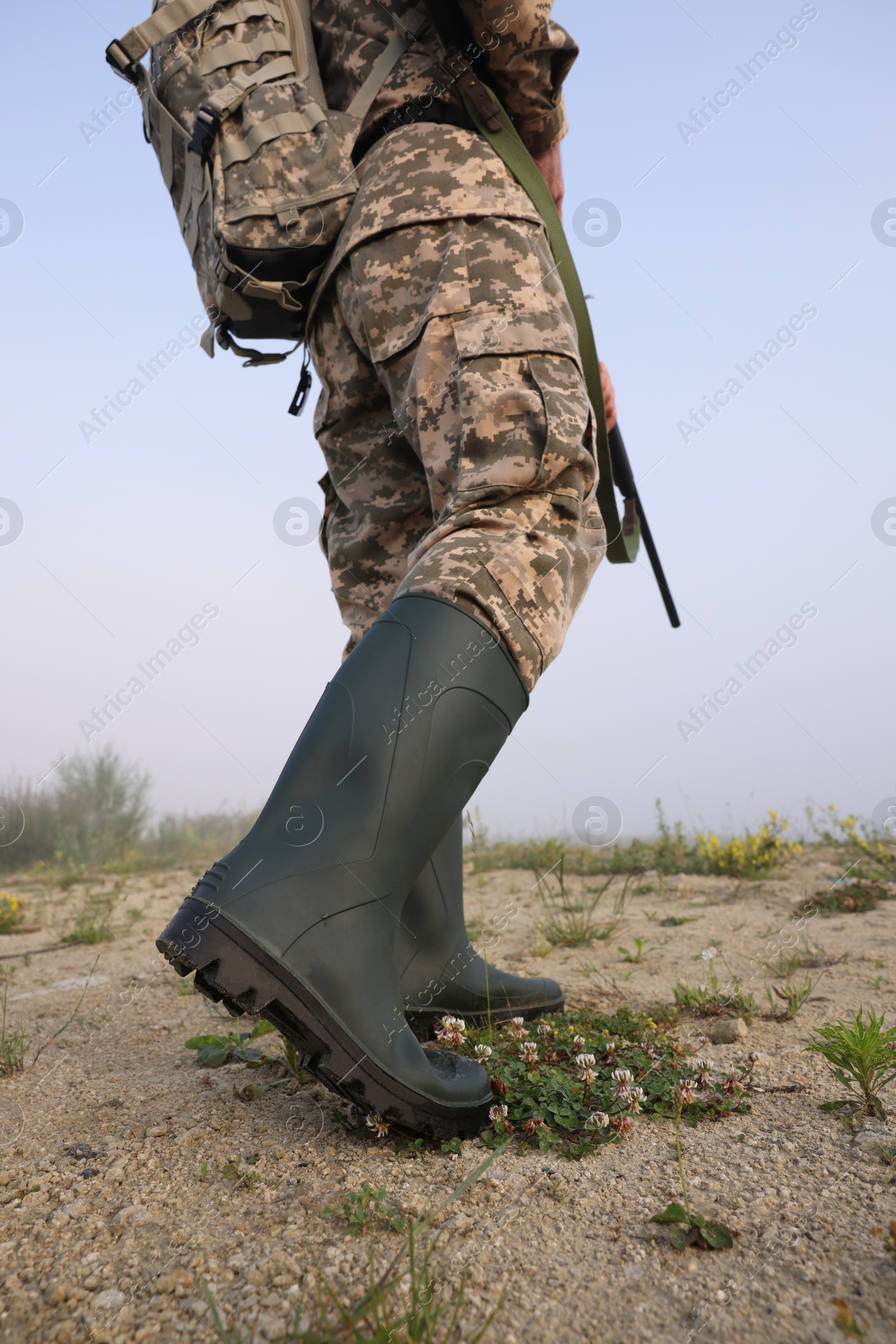 Photo of Man wearing camouflage with hunting rifle and backpack outdoors, closeup