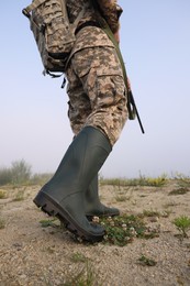 Man wearing camouflage with hunting rifle and backpack outdoors, closeup