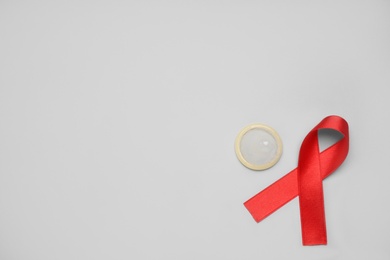 Photo of Red ribbon and condom on light grey background, flat lay with space for text. AIDS disease awareness