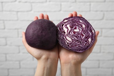 Woman holding dough painted with natural food coloring and red cabbage near white brick wall, closeup