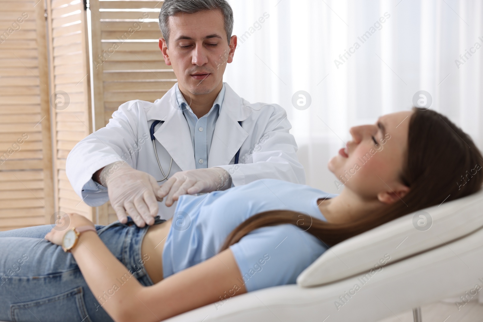 Photo of Gastroenterologist examining patient with stomach pain on couch in clinic