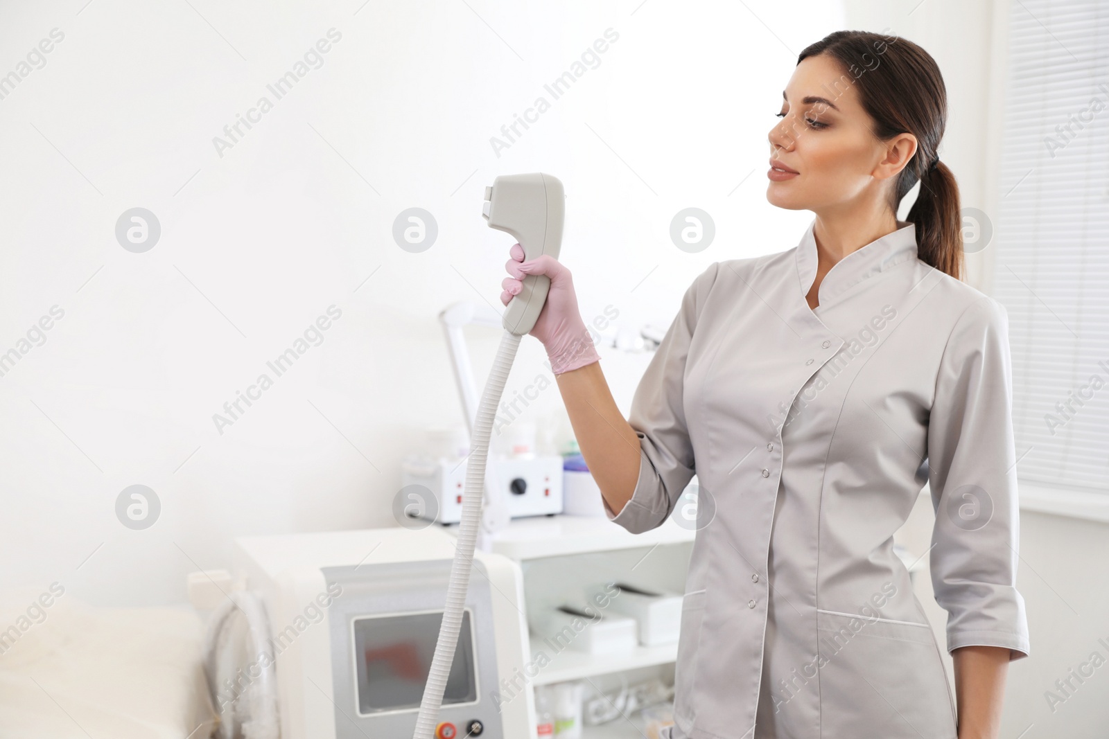 Photo of Young woman holding professional laser epilator in beauty salon