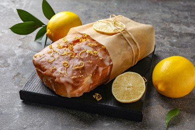Photo of Wrapped tasty lemon cake with glaze and citrus fruits on grey textured table