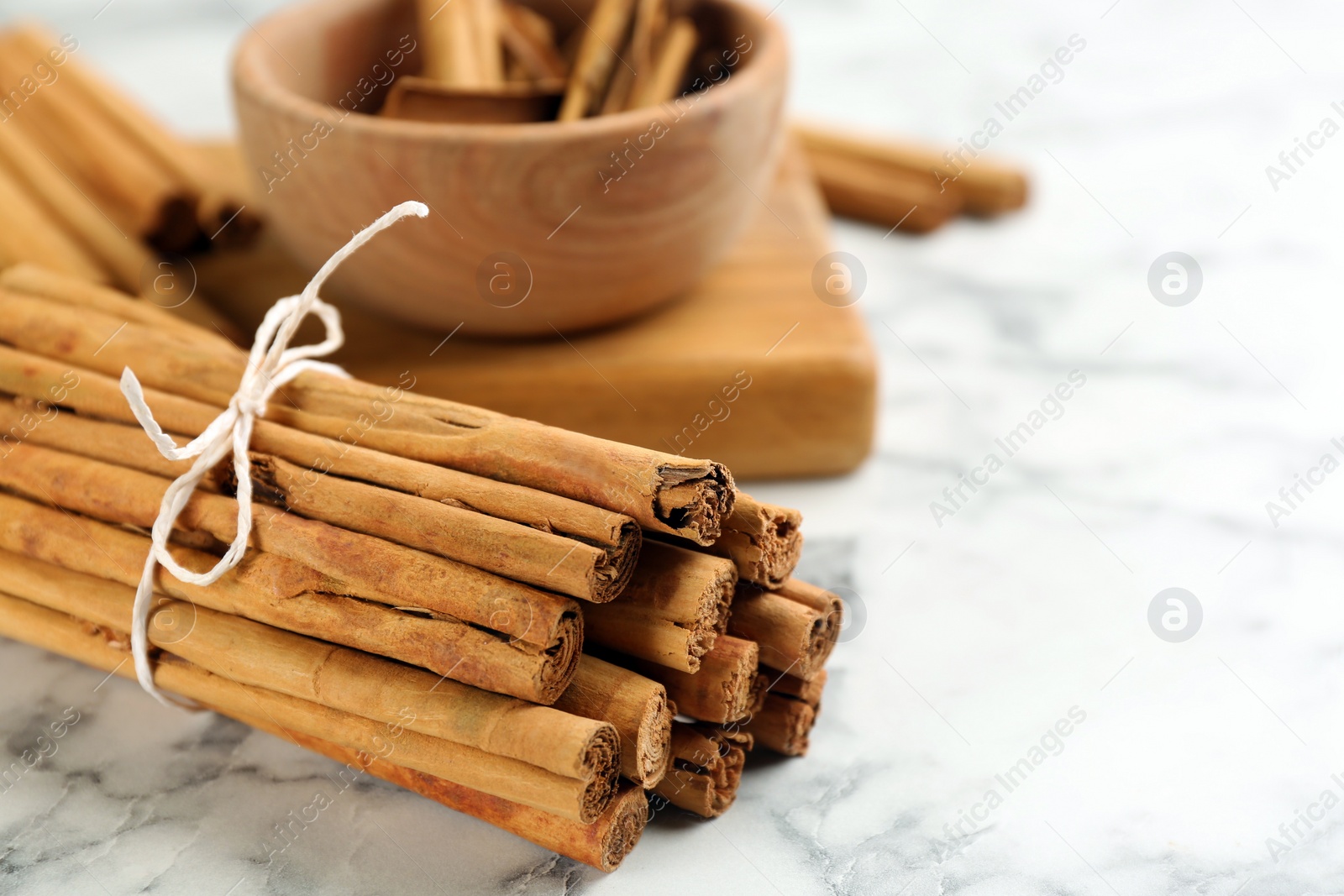Photo of Aromatic cinnamon sticks on white marble table, closeup. Space for text