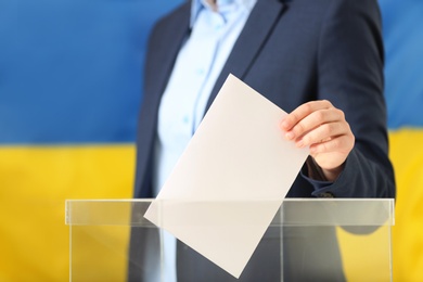 Photo of Woman putting vote into ballot box against Ukrainian flag, closeup. Space for text