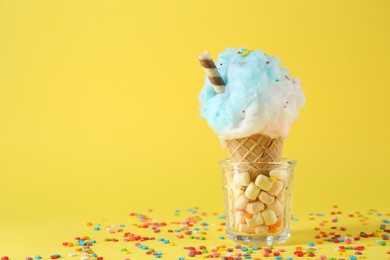 Photo of Sweet cotton candy in waffle cone on yellow background. Space for text