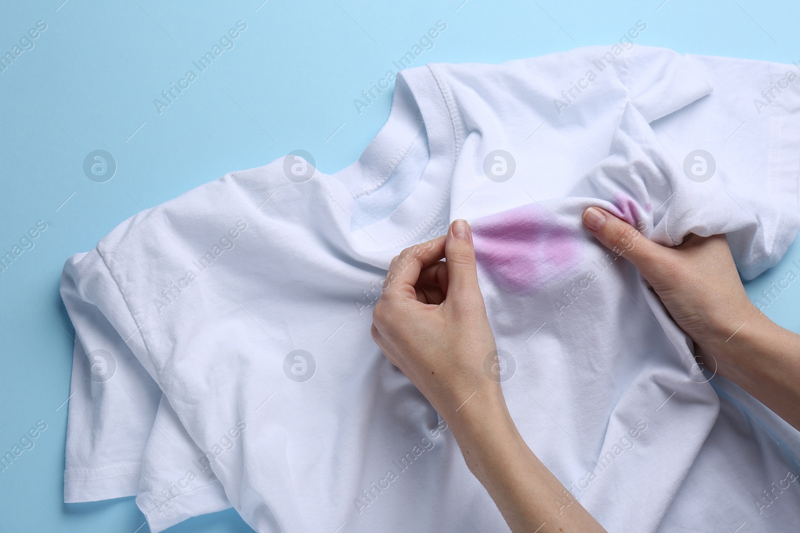 Photo of Woman holding white shirt with purple stains on light blue background, top view