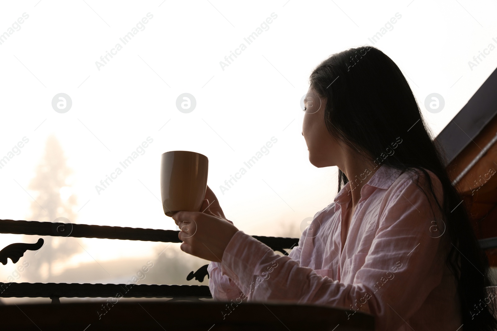 Photo of Young woman sitting at table on balcony with cup of tea in morning