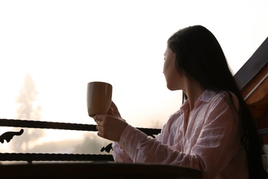 Young woman sitting at table on balcony with cup of tea in morning