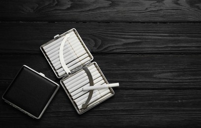 Photo of Stylish leather cigarette cases on black wooden table, flat lay. Space for text