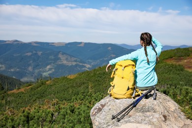 Photo of Tourist with backpack and trekking poles enjoying mountain landscape on rocky peak, back view