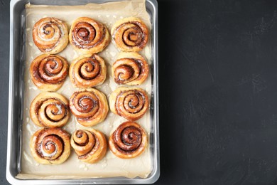 Photo of Baking dish with tasty cinnamon rolls on dark table, top view. Space for text