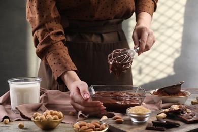 Photo of Woman mixing delicious chocolate cream with whisk at table, closeup