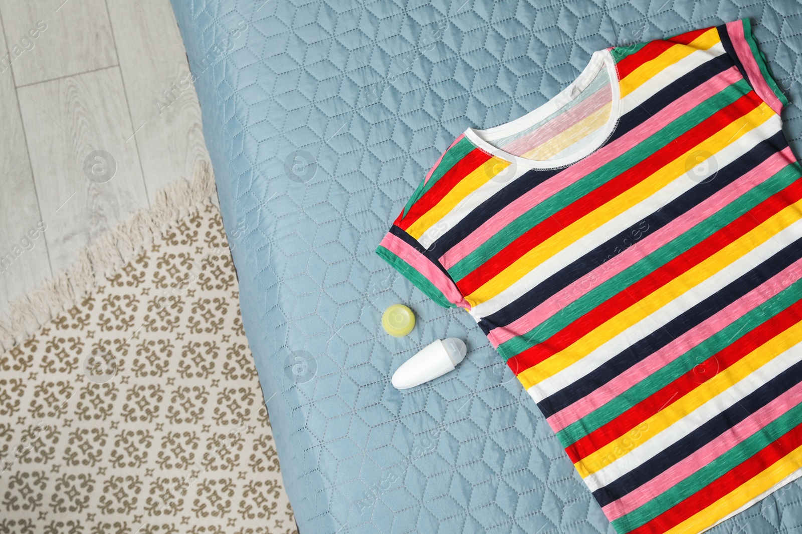 Photo of Female roll-on deodorant and striped t-shirt on bed, top view. Space for text