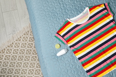 Photo of Female roll-on deodorant and striped t-shirt on bed, top view. Space for text