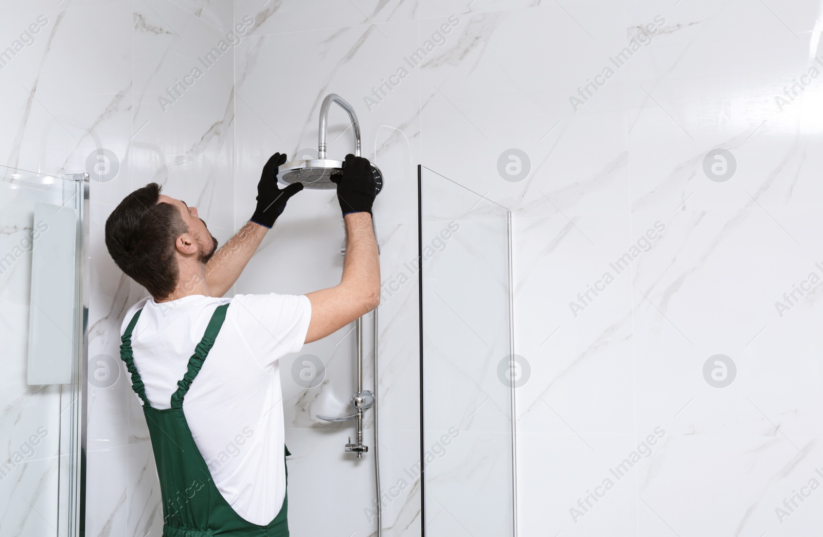 Photo of Professional handyman working in shower booth indoors, space for text