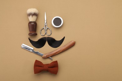 Artificial moustache and barber tools on beige background, flat lay. Space for text