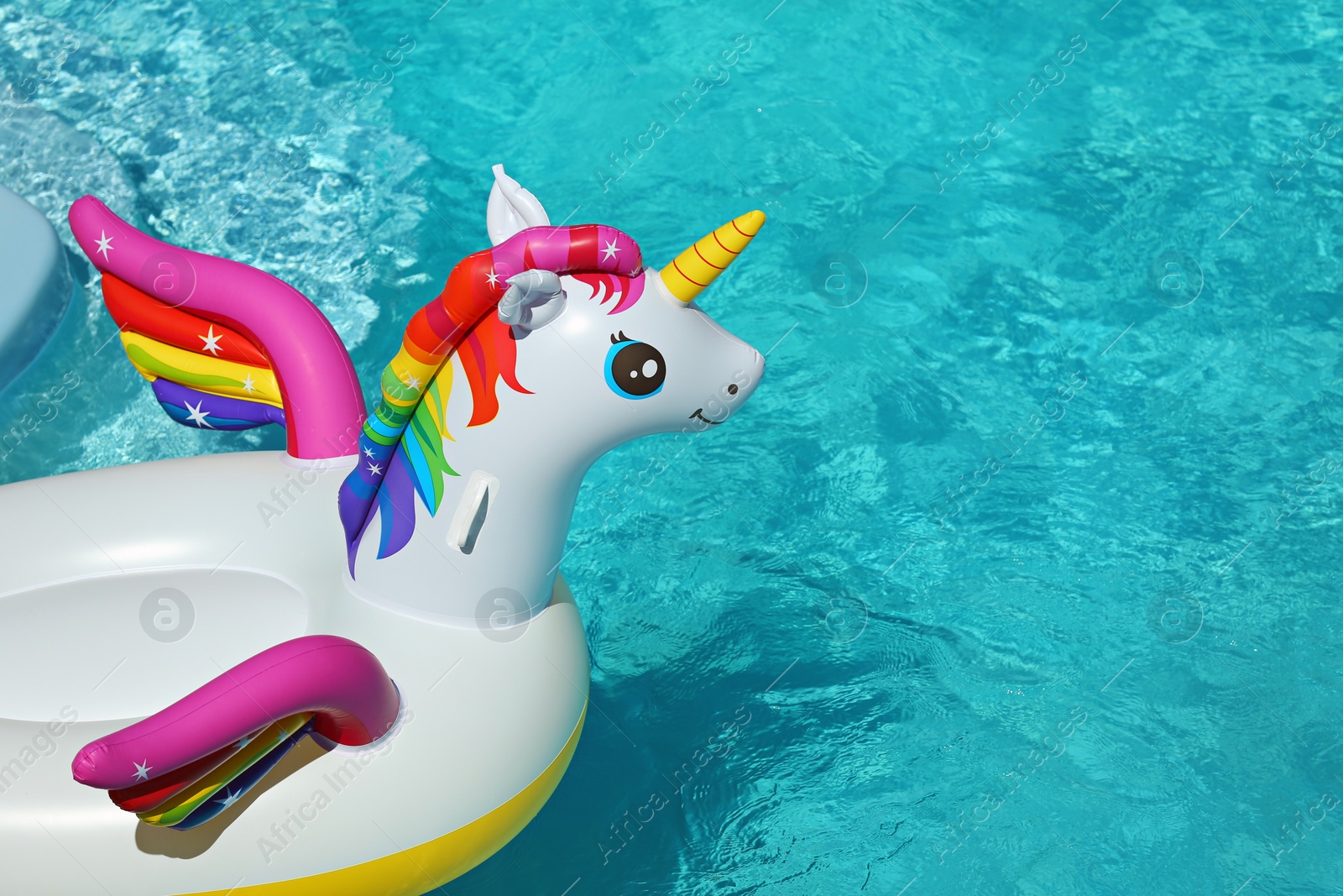 Photo of Funny inflatable unicorn ring floating in swimming pool on sunny day. Space for text