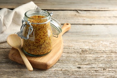 Photo of Whole grain mustard in jar and spoon on wooden table. Space for text