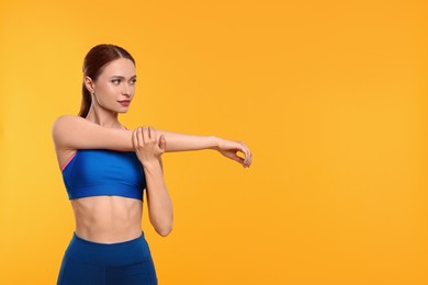 Photo of Young woman in sportswear stretching on yellow background, space for text