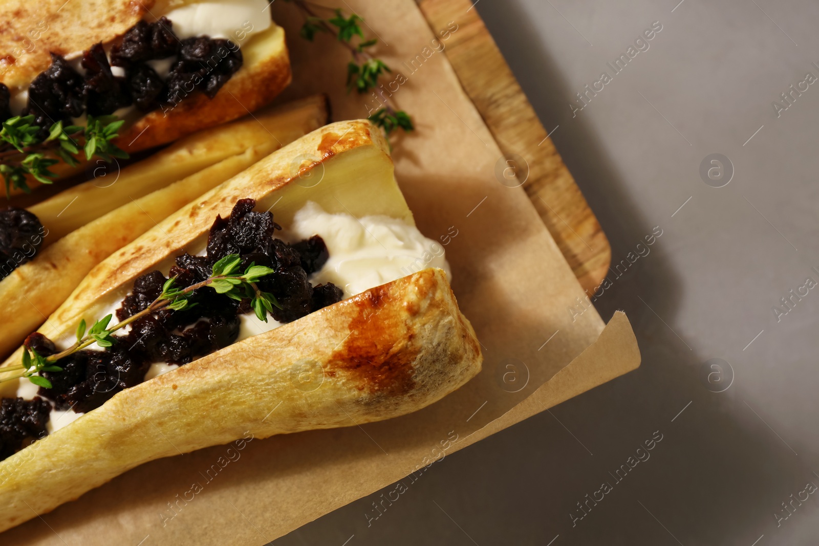 Photo of Tasty baked parsnips with sauce, prunes and thyme on light grey table, closeup. Space for text