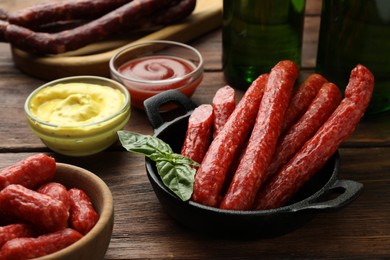 Photo of Thin dry smoked sausages, basil and sauces on wooden table