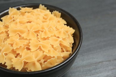 Raw farfalle pasta in bowl on grey table, closeup