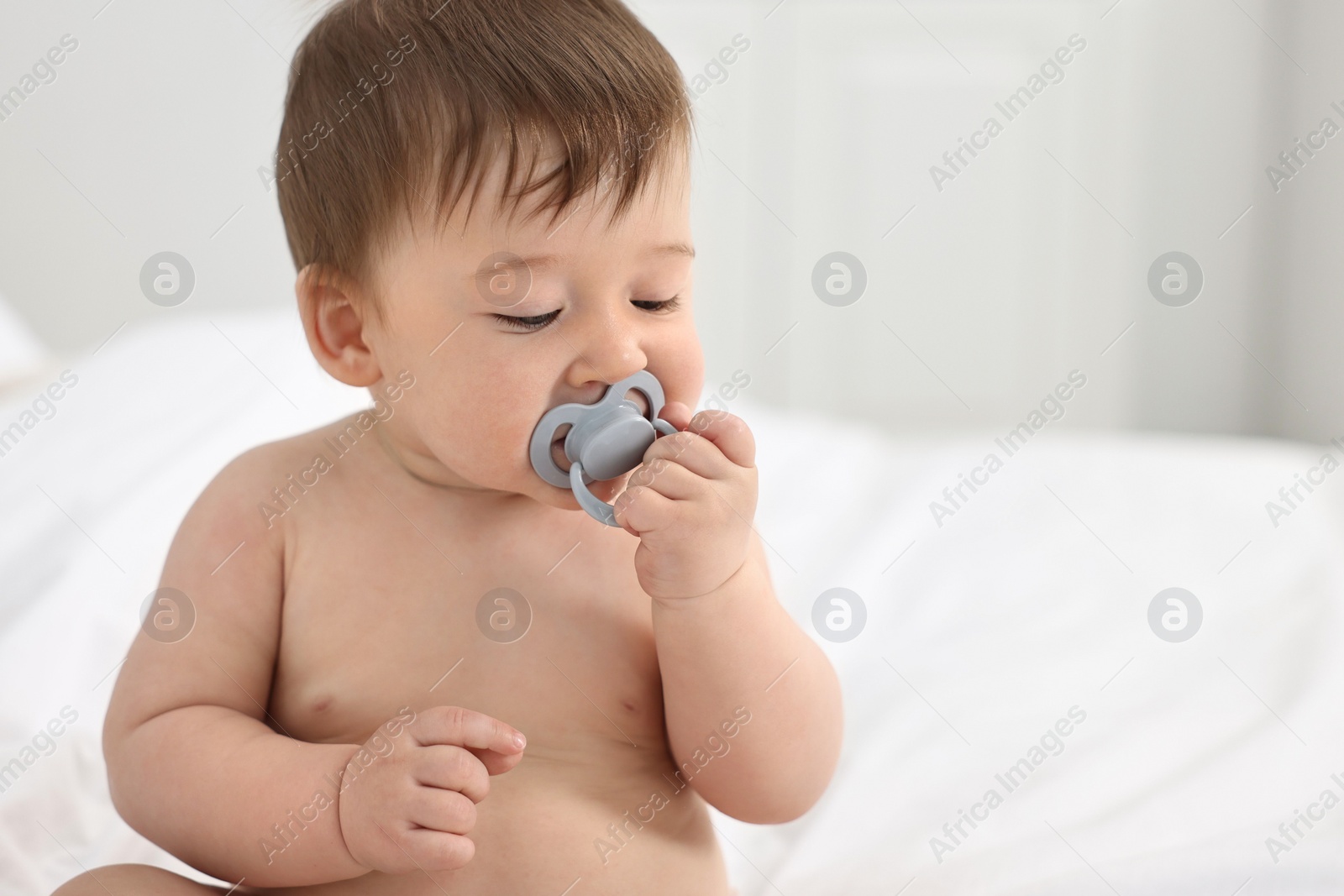 Photo of Cute baby boy with pacifier on bed at home