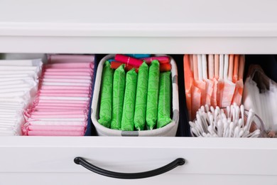 Photo of Open cabinet drawer with menstrual pads, tampons and cotton buds, closeup