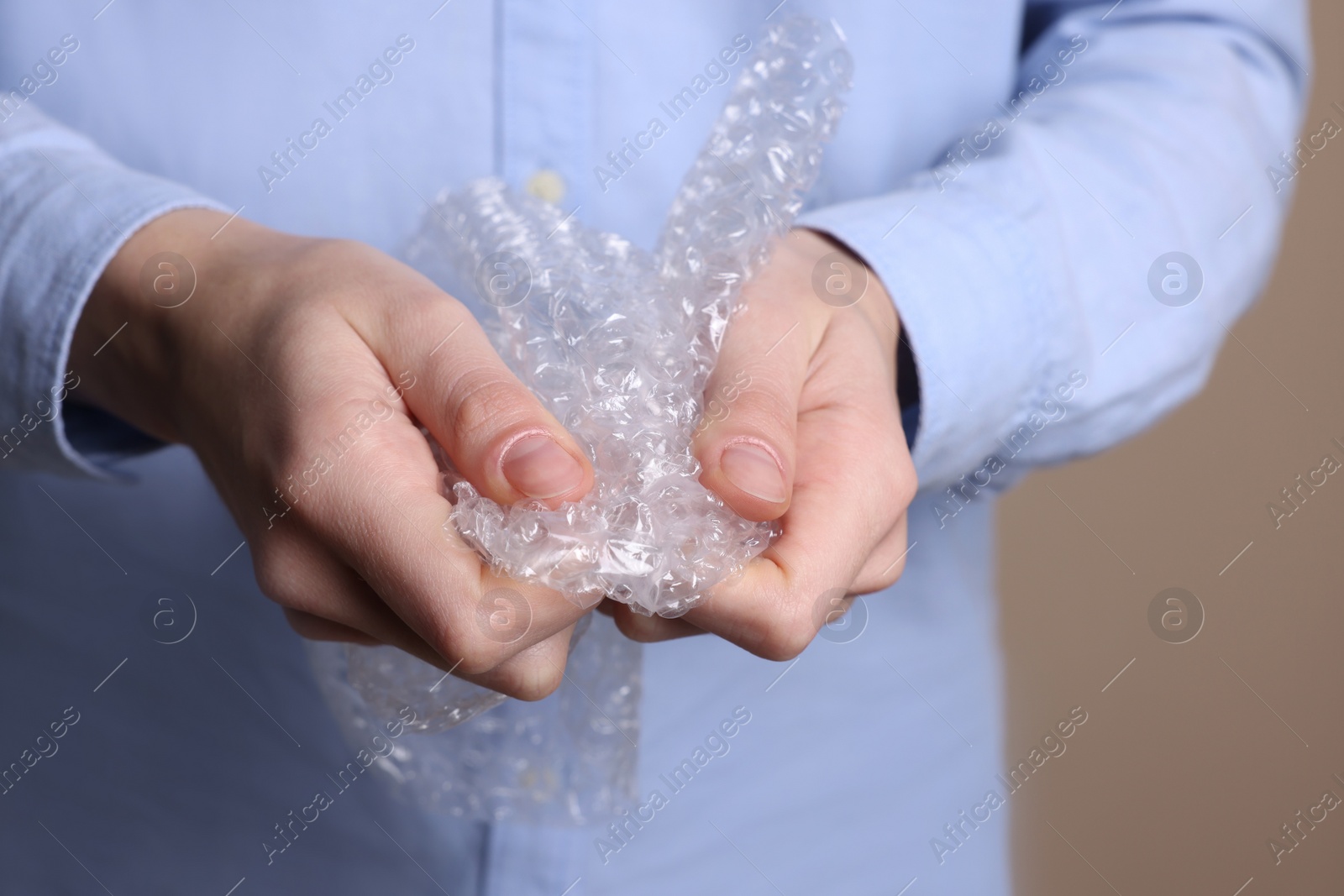 Photo of Woman popping bubble wrap on beige background, closeup. Stress relief