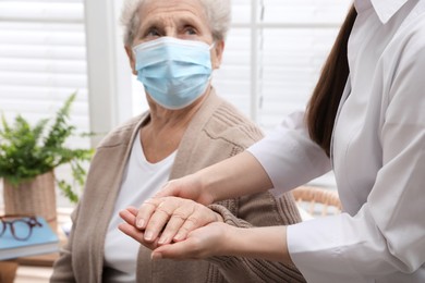 Photo of Doctor taking care of senior woman with protective mask at nursing home, focus on hands