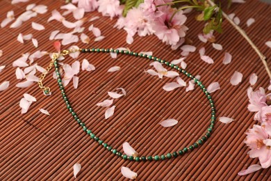 Beautiful blossoming branch, necklace and flower petals on bamboo mat