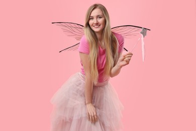 Beautiful girl in fairy costume with wings and magic wand on pink background