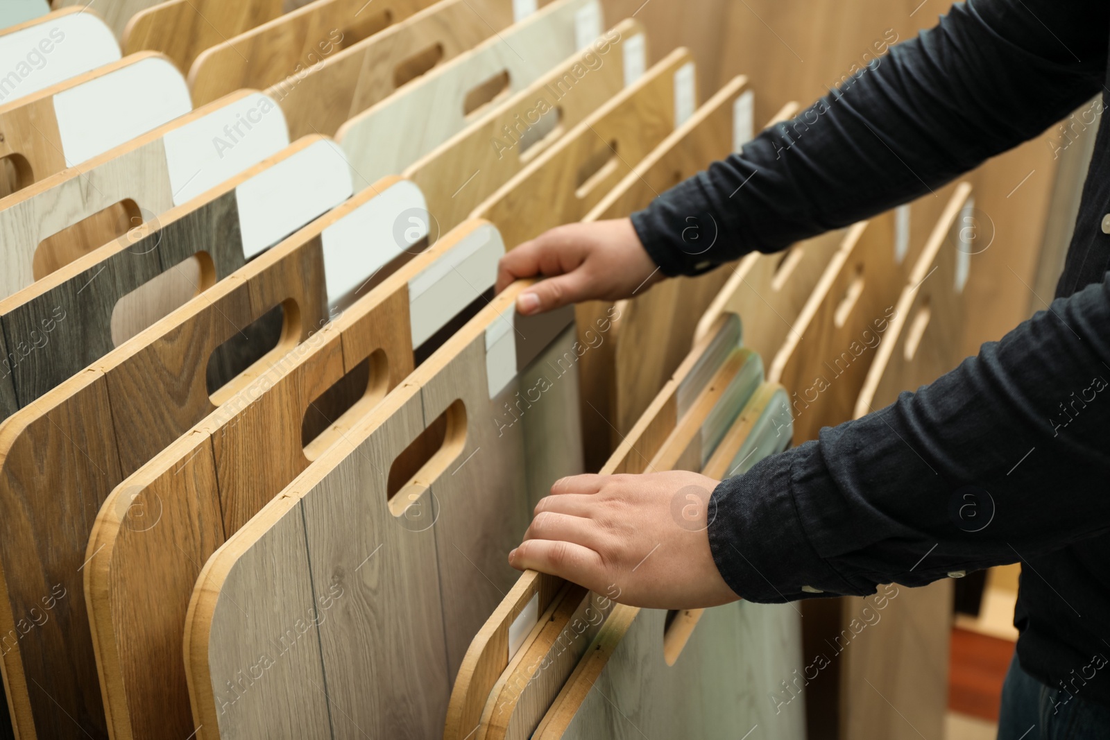 Photo of Man choosing wooden flooring among different samples in shop, closeup