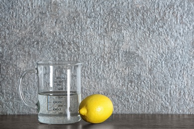 Photo of Measuring cup with vinegar and lemon on grey background. Space for text