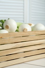 Photo of Crate with green spring onions on white wooden table, closeup
