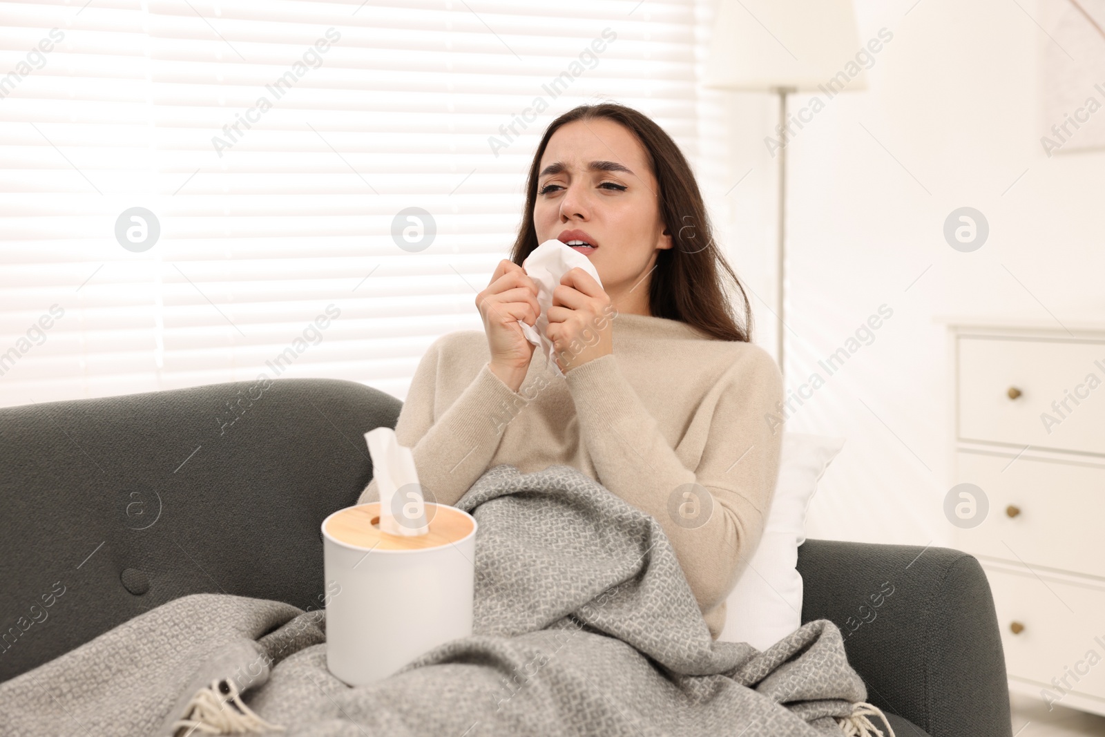 Photo of Sick woman with tissue sneezing on sofa at home. Cold symptoms