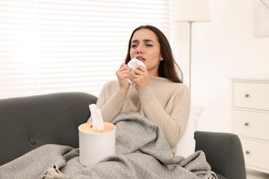 Photo of Sick woman with tissue sneezing on sofa at home. Cold symptoms