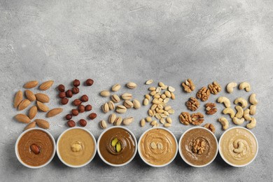 Photo of Tasty nut butters in bowls and raw nuts on light grey background, flat lay