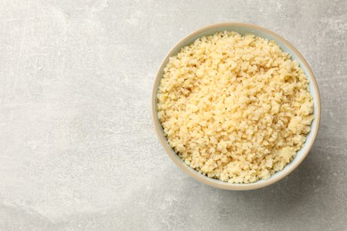 Photo of Delicious bulgur in bowl on light grey table, top view. Space for text