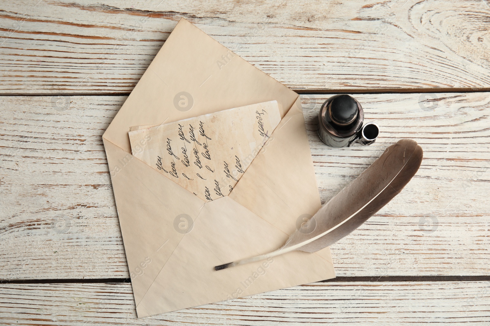 Photo of Feather pen, bottle of ink and letter on white wooden table, flat lay