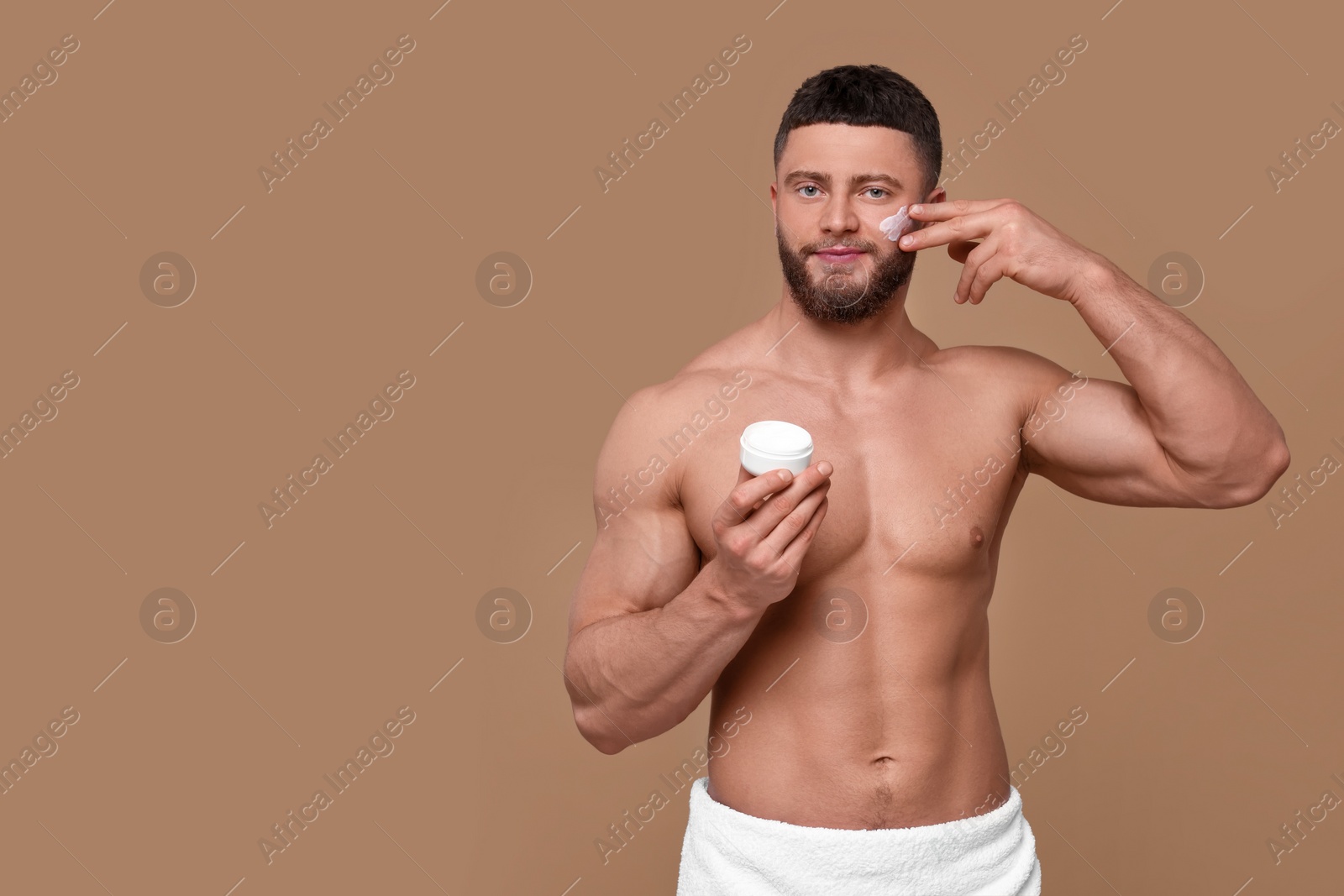 Photo of Handsome man applying cream onto his face on pale brown background, space for text