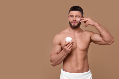 Handsome man applying cream onto his face on pale brown background, space for text